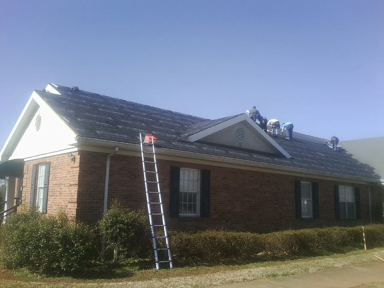 Crew tearing shingles off a brick ranch roof with a ladder set — Metal Roof Repair work by our crew in Ipava
