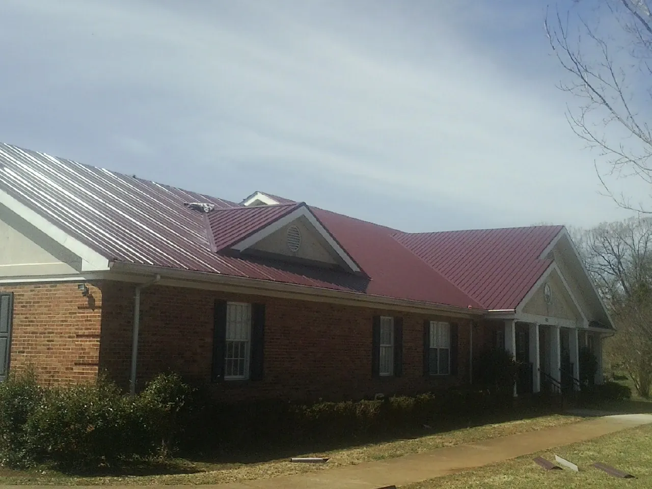Red metal roof with gabled entries on a long brick building, from a Hail Damage Roof Repair job in Ipava