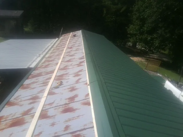 Old rusted panels beside newly installed green metal roofing — Wind Damage Roof Repair by Roofing Brothers in Ipava