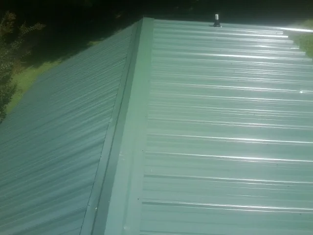 New green metal panels meeting at the ridge of a roof — Flat Roof Repair work by our crew in Ipava