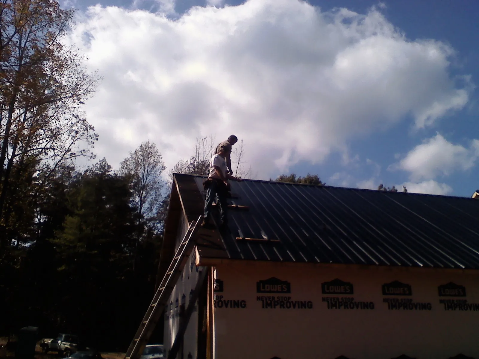 Roofer fastening dark metal panels high against a cloudy sky, from a Roof Inspection job in Ipava